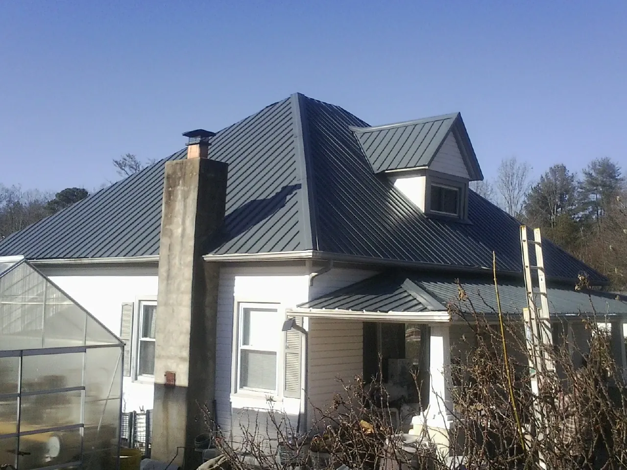 Dark blue standing seam metal roof on a white farmhouse with dormer — Slate & Tile Roof Repair by Roofing Brothers in Polk