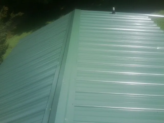 New green metal panels meeting at the ridge of a roof — Flat Roof Repair work by our crew in Polk